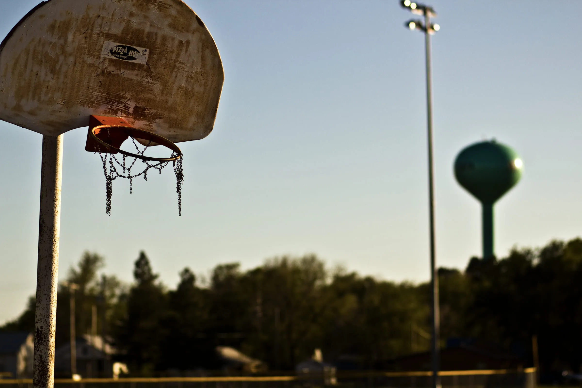 A weathered basketball backboard and netless hoop against the sky, a water tower behind it