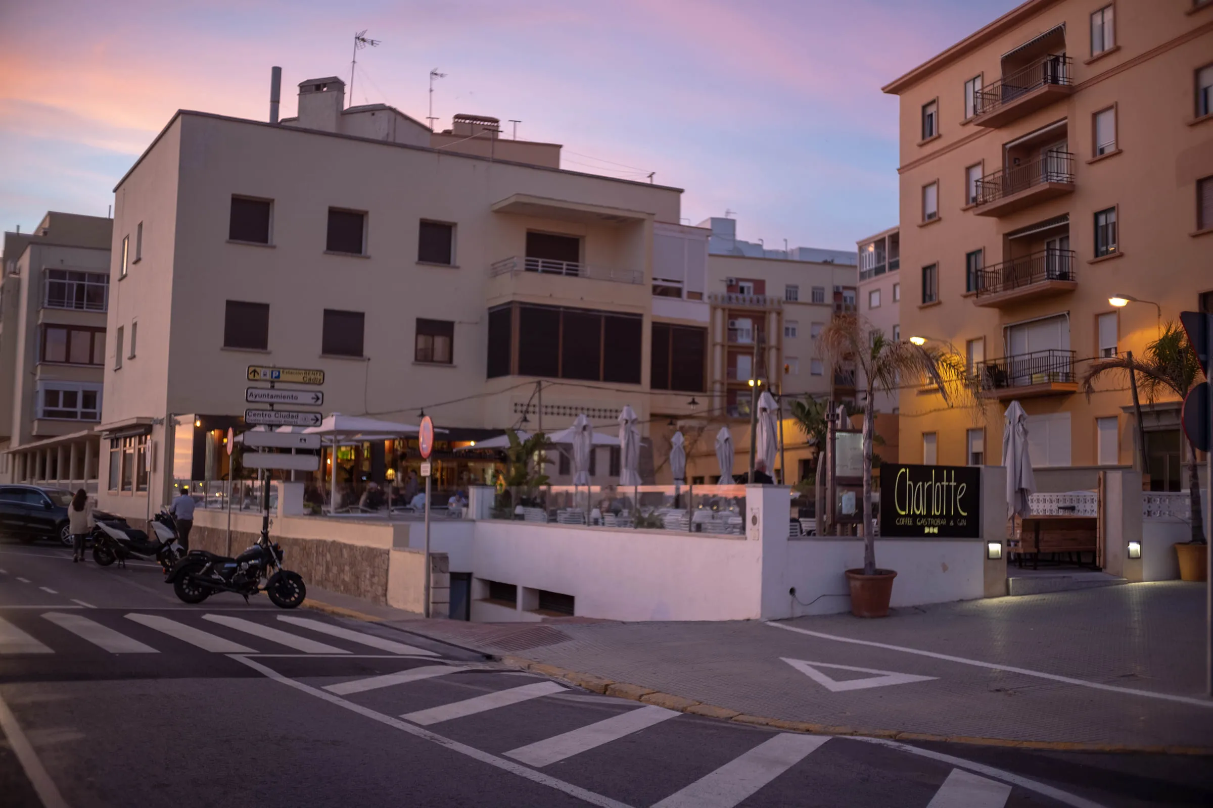 A quiet street corner at dusk, a bar signed Charlotte on the ground floor of an apartment block