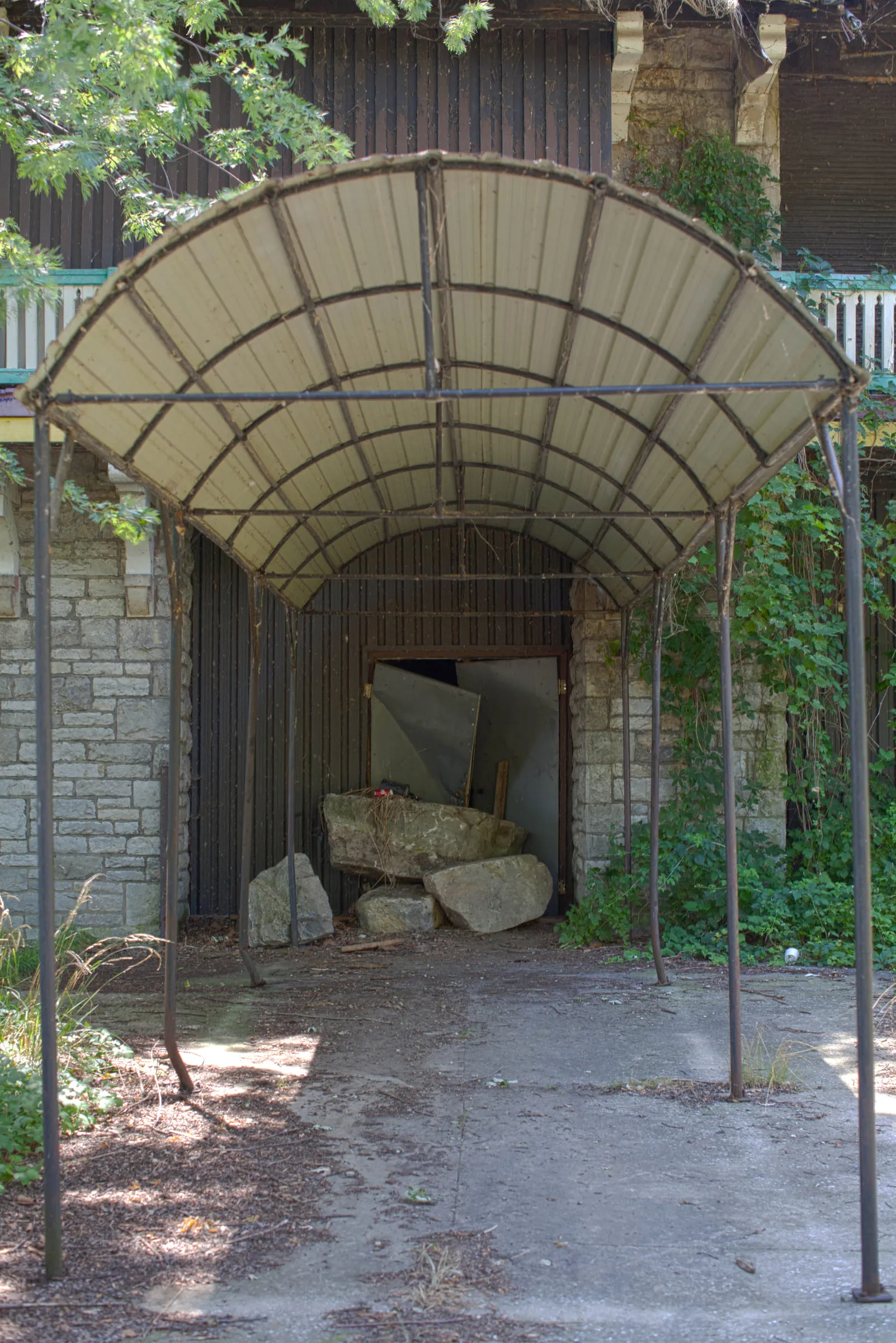 A rusted metal canopy frame over a boarded stone doorway, broken masonry piled inside