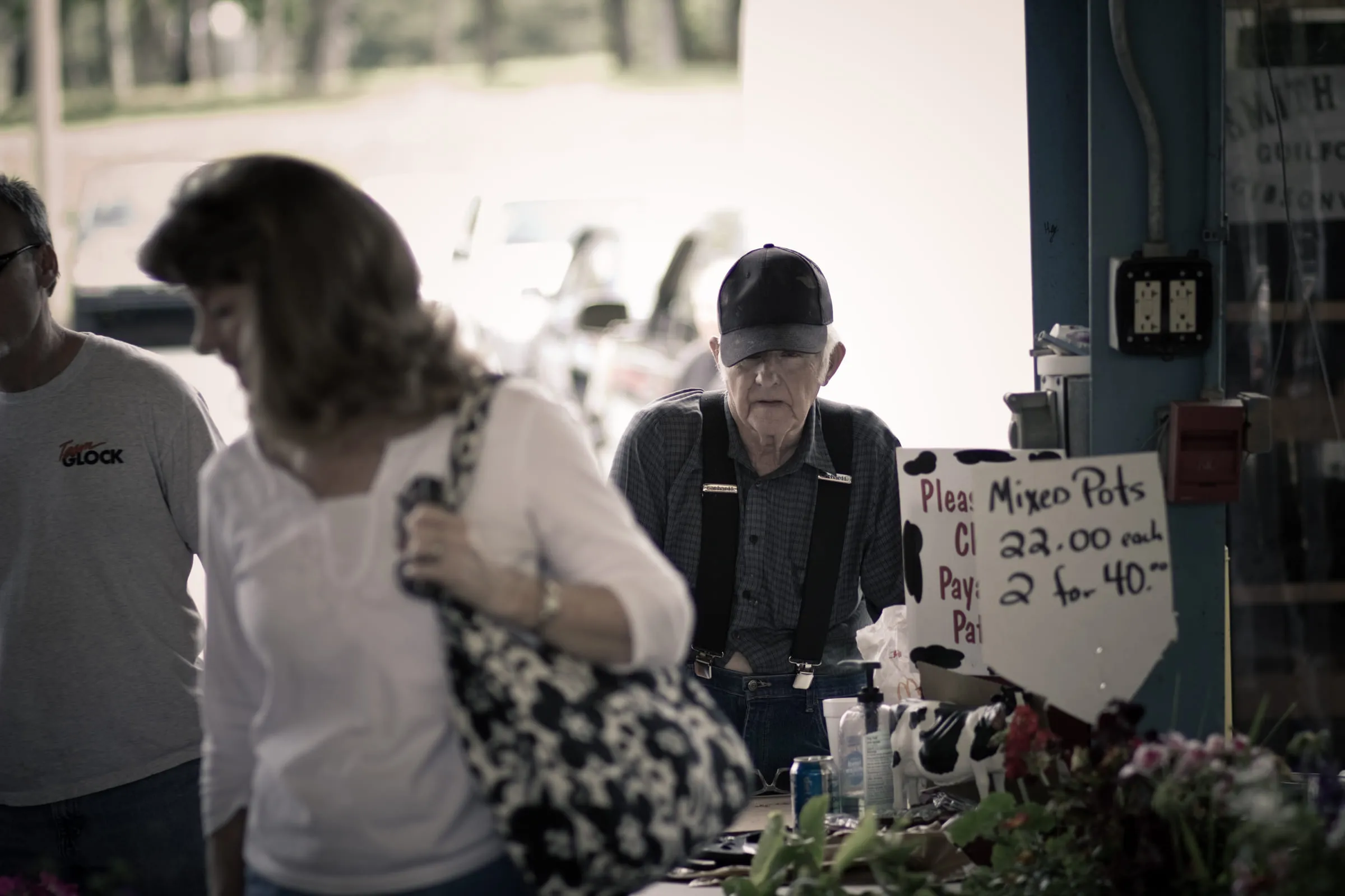 Shoppers at a plant stall, a handwritten sign reading "Mixed Pots" propped on the table