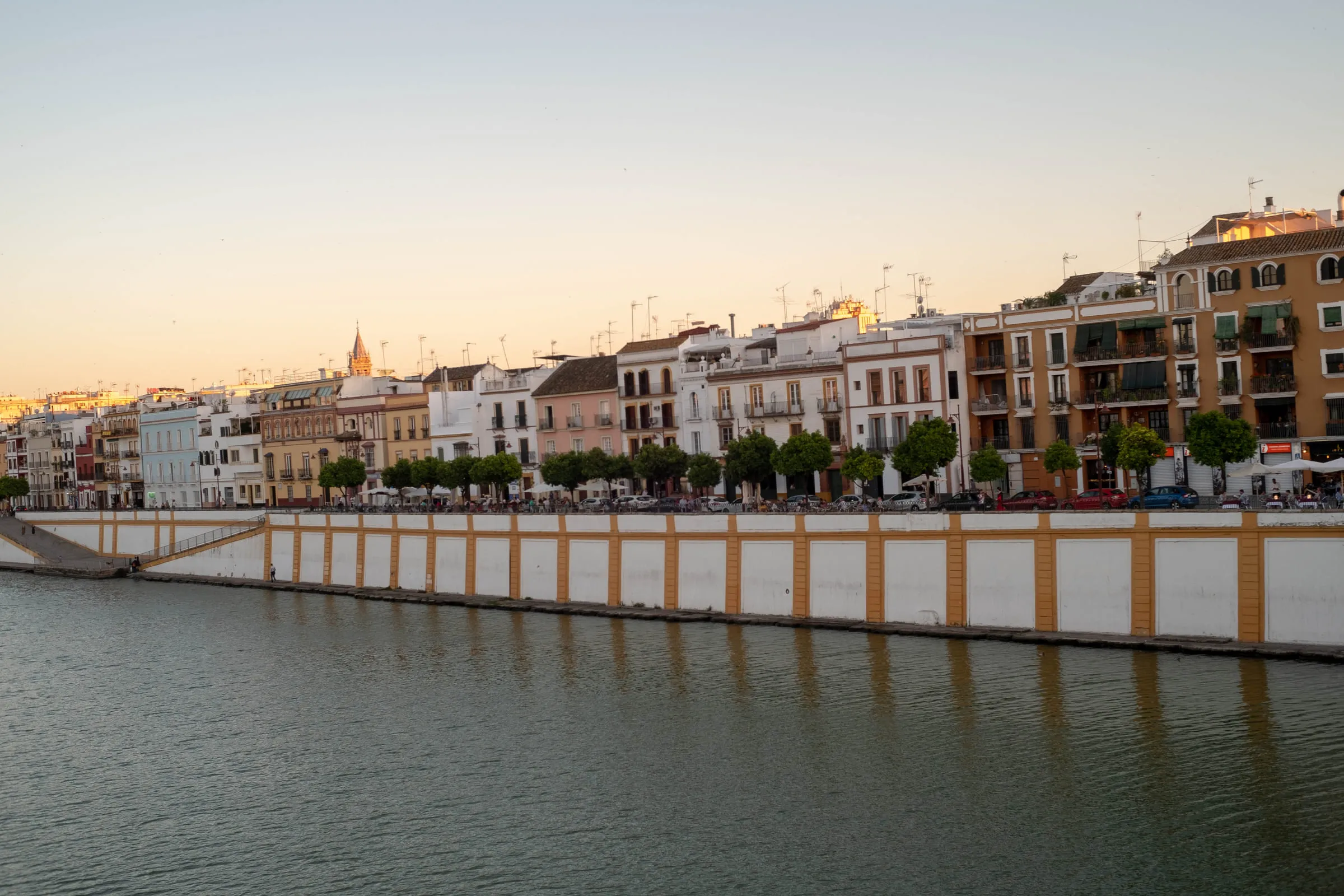 Pale townhouses lining the Guadalquivir at dusk, their pilings reflected in still water