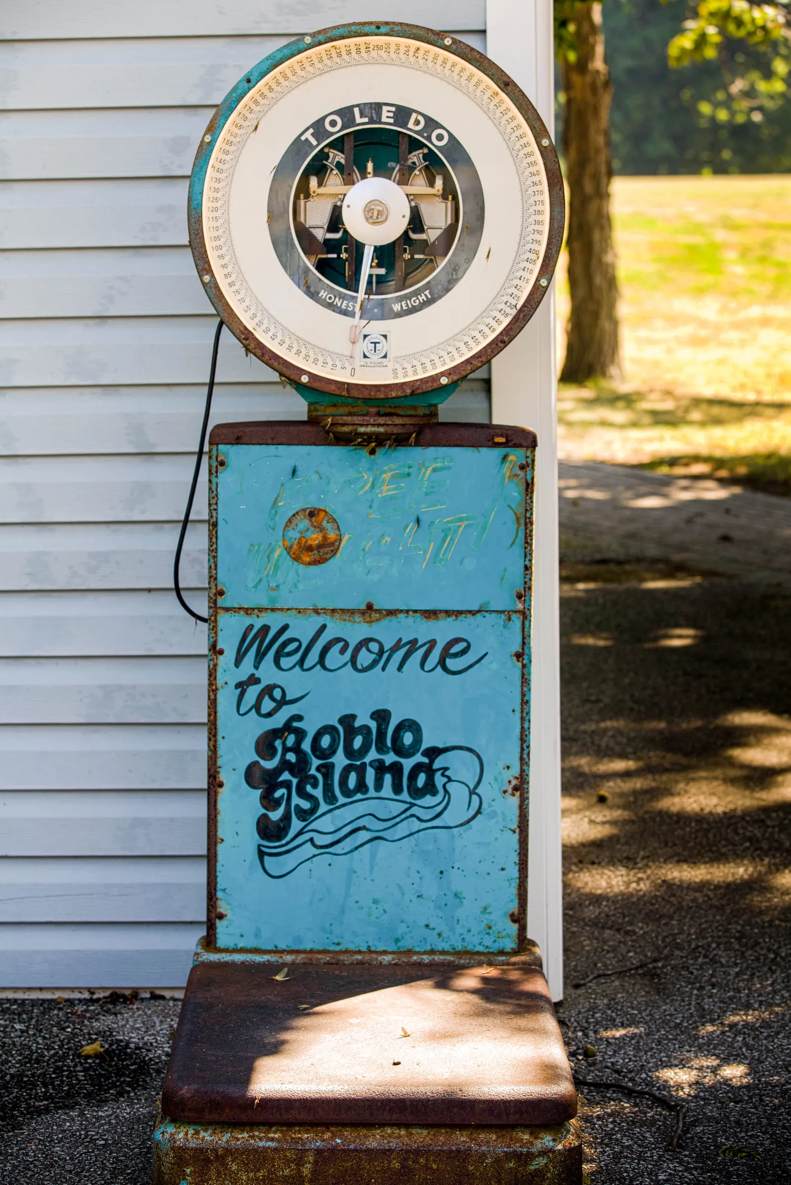 An old Toledo platform scale painted with the Welcome to Boblo Island lettering, standing against a clapboard wall