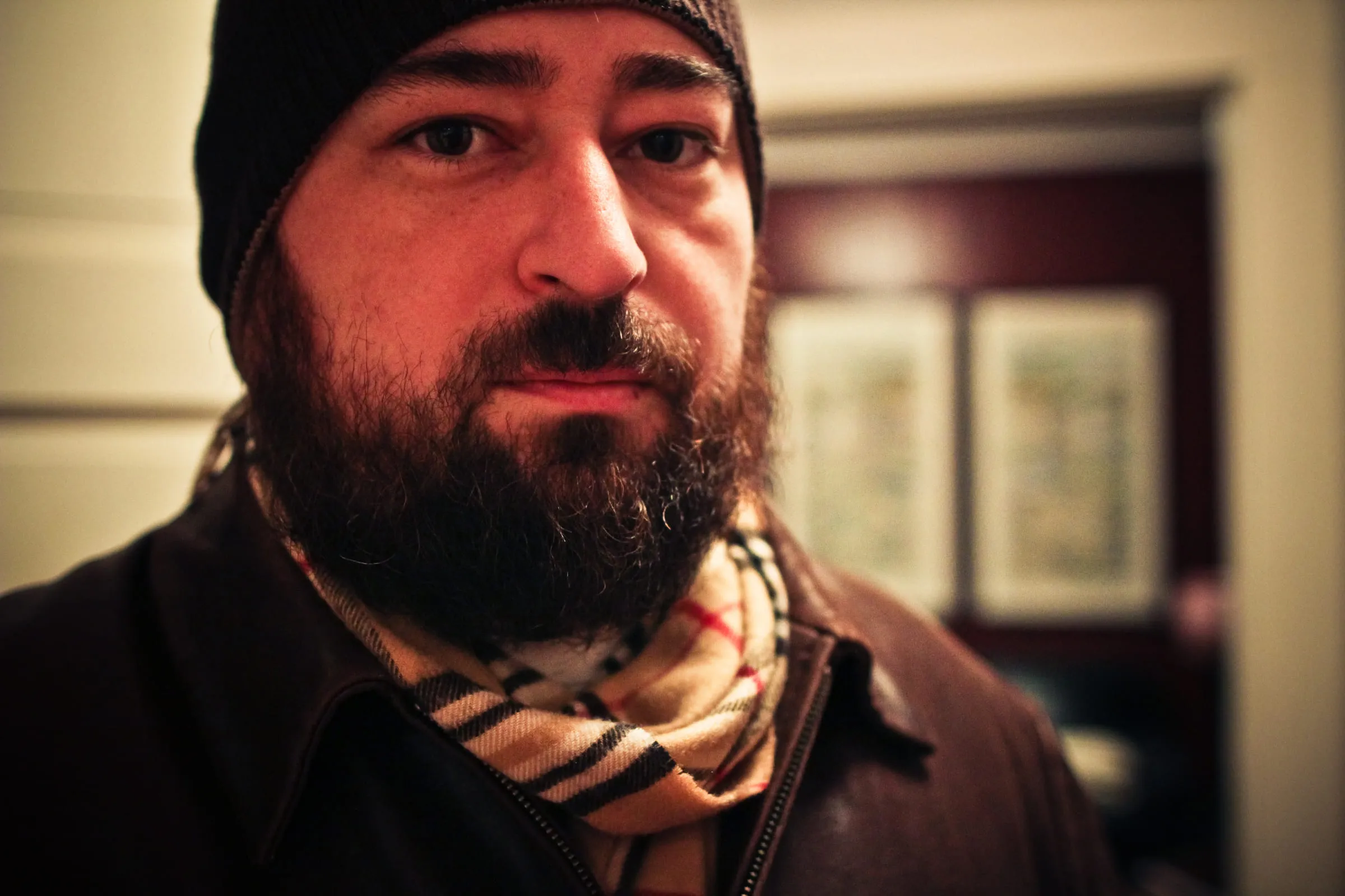 Self-portrait in a beanie and scarf, indoors against a pale wall